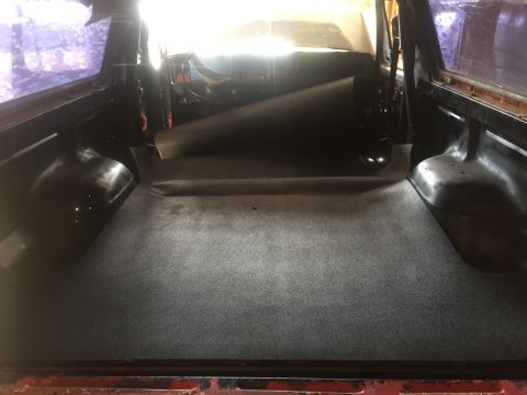 1978 Ford Bronco - The cargo area of a 1978 Ford Bronco shows grey carpeting and a dark rolled-up mat.