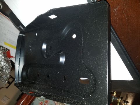 1971 Ford Mustang - A black metal battery tray is shown, likely for a vehicle, with various holes and stamped features.