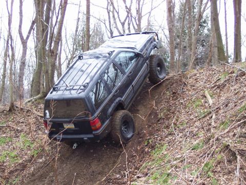 1978 Ford Bronco - A black SUV navigates a steep, wooded incline with its tires angled on the dirt.