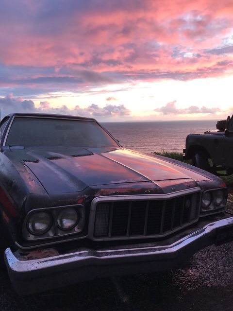 1974 Ford Ranchero - A 1974 Ford Ranchero sits by the ocean as the sun sets, casting colorful hues across the sky and the vehicle's hood.