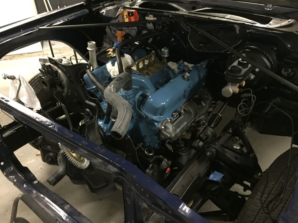 Engine bay with a blue painted V8 engine, dark blue frame, and tire visible
