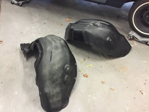 2001 Ford Crown Victoria - Two black plastic fender liners are shown on a concrete floor, with a partial vehicle tire visible in the background.