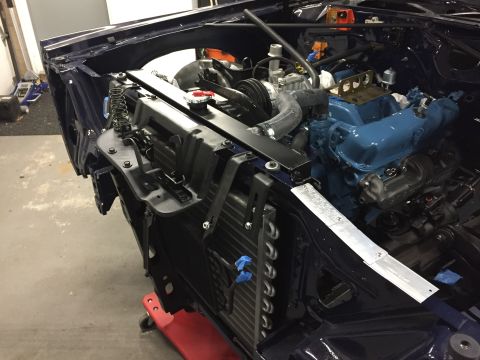 2001 Ford Crown Victoria - Engine bay of a dark blue car, showing the blue-painted engine, radiator, and AC condenser during assembly.