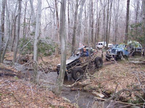 1978 Ford Bronco - Off-road vehicles traverse a stream bed in a wooded area during an outing.
