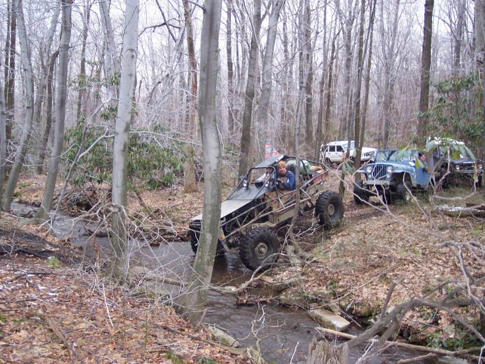 Several off-road vehicles, including a buggy and jeeps, navigate a wooded stream