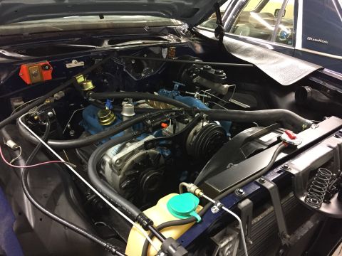 2001 Ford Crown Victoria - The engine bay of a dark blue vehicle, showing the engine and various hoses and components. A second vehicle is partially visible in the ba…
