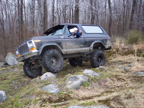 1978 Ford Bronco - A 1978 Ford Bronco navigates a rocky trail in a forest, its off-road capabilities.