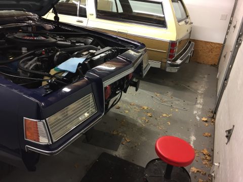 2001 Ford Crown Victoria - Two cars are parked inside a garage, one with its hood up, revealing the engine.