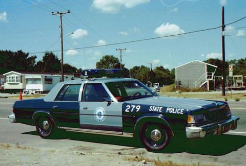 2001 Ford Crown Victoria - A police car with a light bar on the roof is parked on the side of the road.