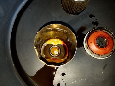 2000 Ford Crown Victoria - A used oil filter housing sits next to a new oil filter, with spilled oil visible.