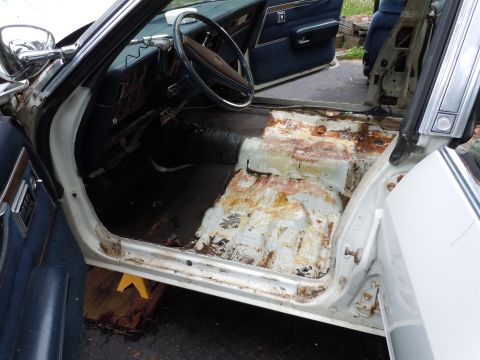 2001 Ford Crown Victoria - Car interior stripped down, revealing significant rust damage on the floor pans.