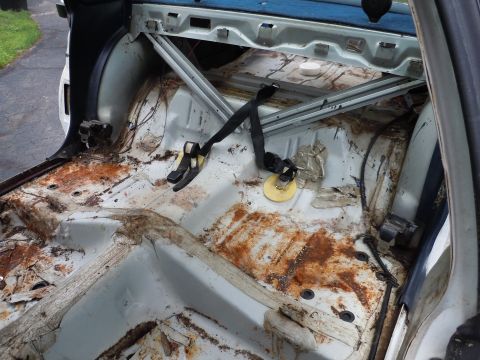 2001 Ford Crown Victoria - The interior of a car is shown with seats removed, revealing significant rust and exposed metal components.