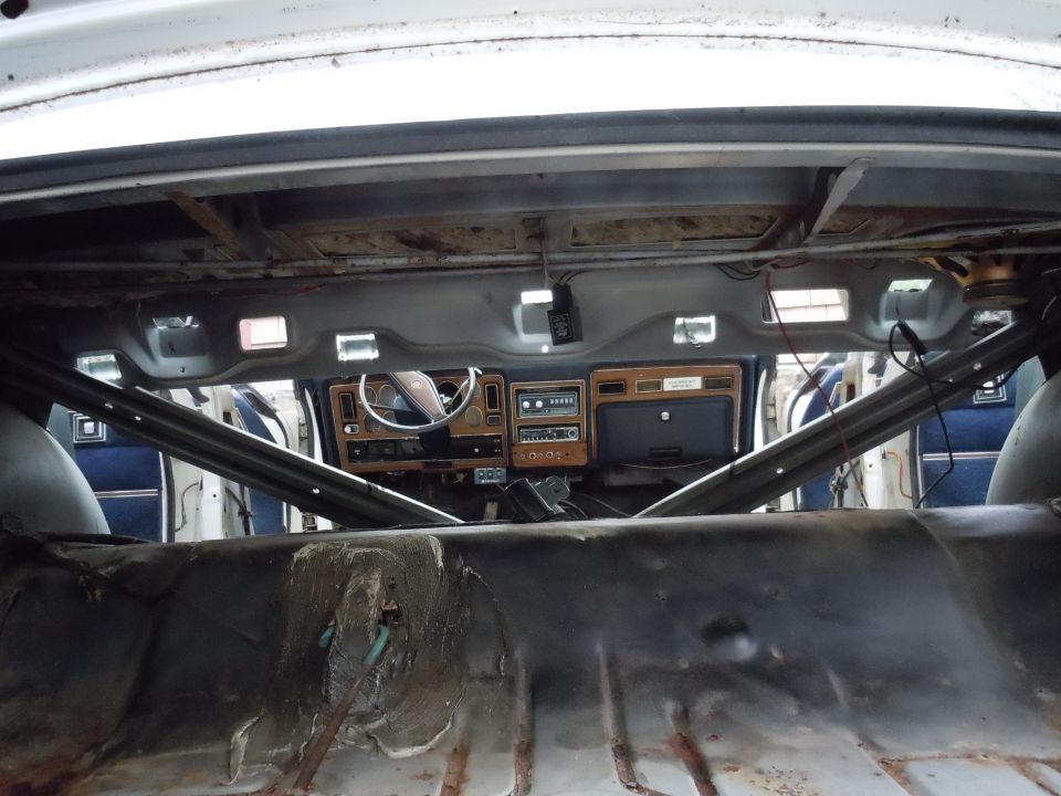 Interior of a stripped-down car, showing exposed metal floor, roll cage, and dashboard with wood trim