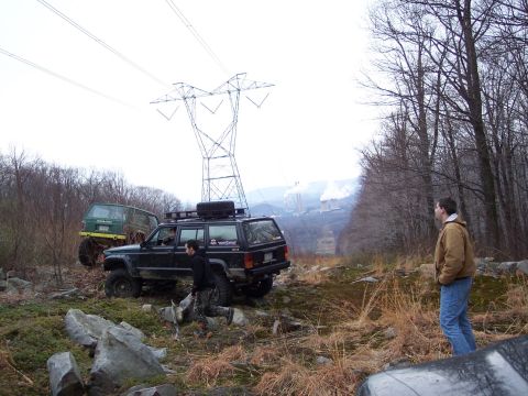 1978 Ford Bronco - Two SUVs navigate a rocky, wooded terrain under a large power line tower.