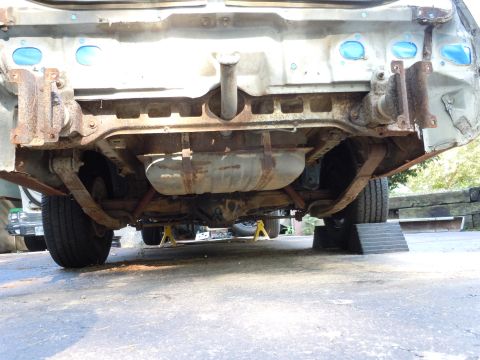 2001 Ford Crown Victoria - The rear undercarriage of a vehicle is visible, a fuel tank, leaf springs, and extensive rust on the frame.