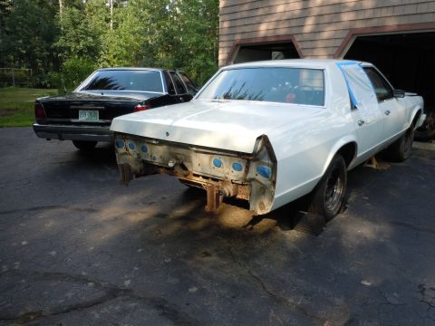 2001 Ford Crown Victoria - Two sedans parked in a driveway, one undergoing repairs with its rear end disassembled.