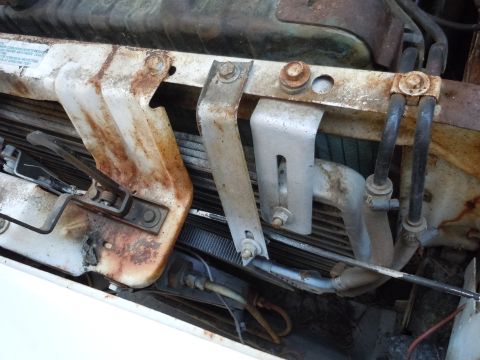 2001 Ford Crown Victoria - Close-up of rusted radiator support brackets and hoses in an engine bay.
