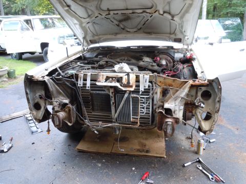 2001 Ford Crown Victoria - Disassembled front end of a white vehicle, revealing the engine and radiator. Tools are scattered on the ground nearby.