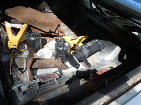 2001 Ford Crown Victoria - The trunk of a vehicle is filled with assorted parts and debris, including yellow jack stands and rusty metal pieces.
