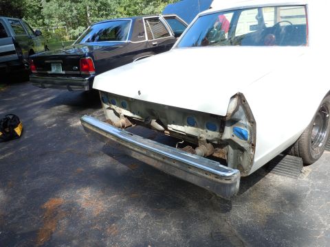 2001 Ford Crown Victoria - A white car with its front end disassembled sits in a driveway next to a black sedan.