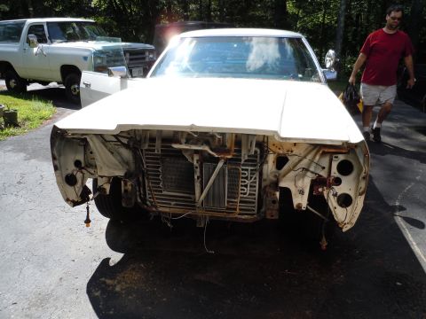 2001 Ford Crown Victoria - A white car sits with its front end disassembled, revealing the radiator and other engine parts. A white truck is parked behind it.