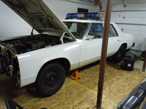2001 Ford Crown Victoria - White police car on jack stands in a garage with hood open, revealing the engine.