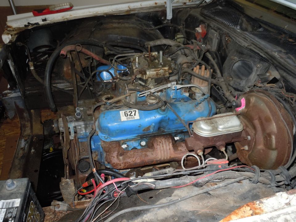 Engine bay showing a blue engine block, carburetor, brake booster, and wiring. A sticker with '627' is visible on the engine