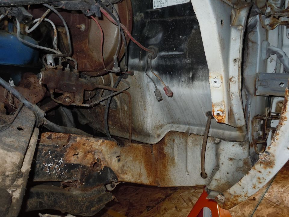 Close-up of rusty engine bay components and frame structure with wiring harnesses visible