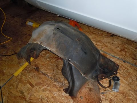 2001 Ford Crown Victoria - A rusty fender liner, likely from a vehicle, is shown with a small motor and ring attached.