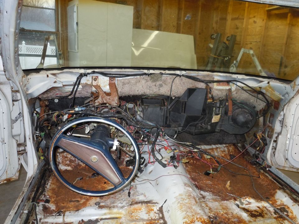 Disassembled car interior showing exposed wiring, rusted floor, and dashboard components