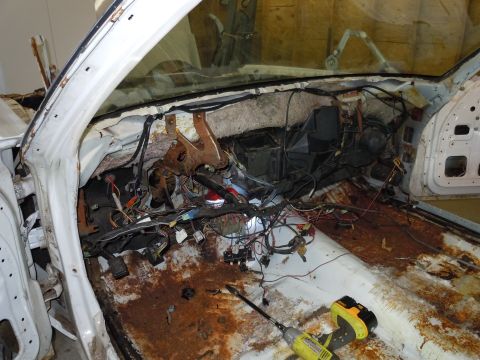 2001 Ford Crown Victoria - The interior of a car is shown with extensive wiring exposed and significant rust on the floor panels, indicating a state of disrepair.