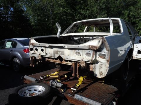 2001 Ford Crown Victoria - The stripped-down body of a car is loaded onto a trailer, with another vehicle visible in the background.