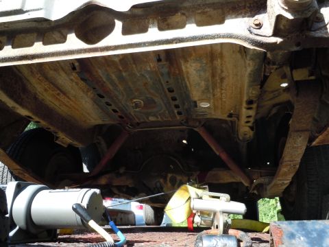 2001 Ford Crown Victoria - The heavily rusted underbody of a vehicle is shown from a low angle, with visible suspension and exhaust parts.