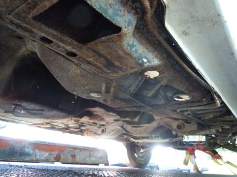 2001 Ford Crown Victoria - The undercarriage of a vehicle displays significant rust and wear, with suspension parts and a tire visible.