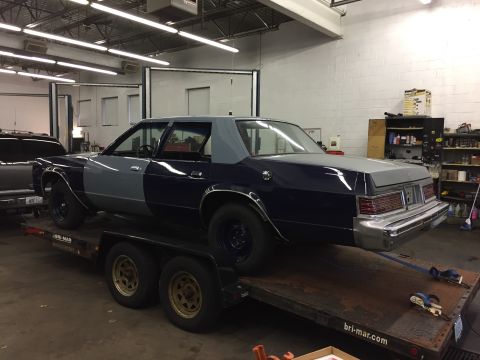 2001 Ford Crown Victoria - A two-tone sedan, dark blue and grey, is loaded onto a trailer inside a garage.