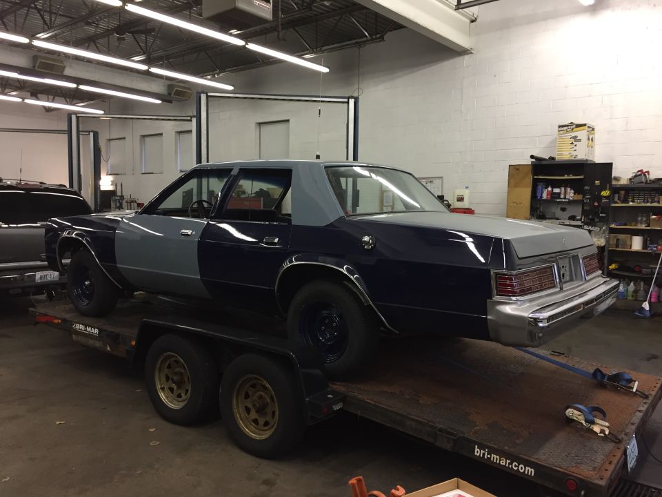 Dark blue and grey sedan on a trailer, rear 3/4 view