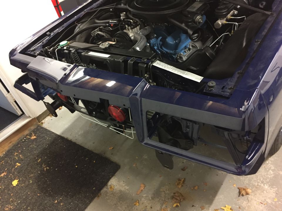 Dark blue car's engine bay and front clip, missing headlights and grille. Blue engine block visible