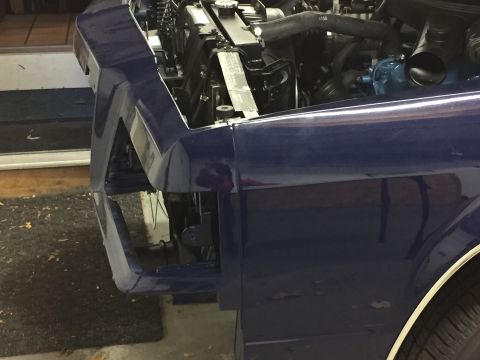 2001 Ford Crown Victoria - Close-up view of the front fender and engine compartment of a blue vehicle, showing the radiator and various hoses.