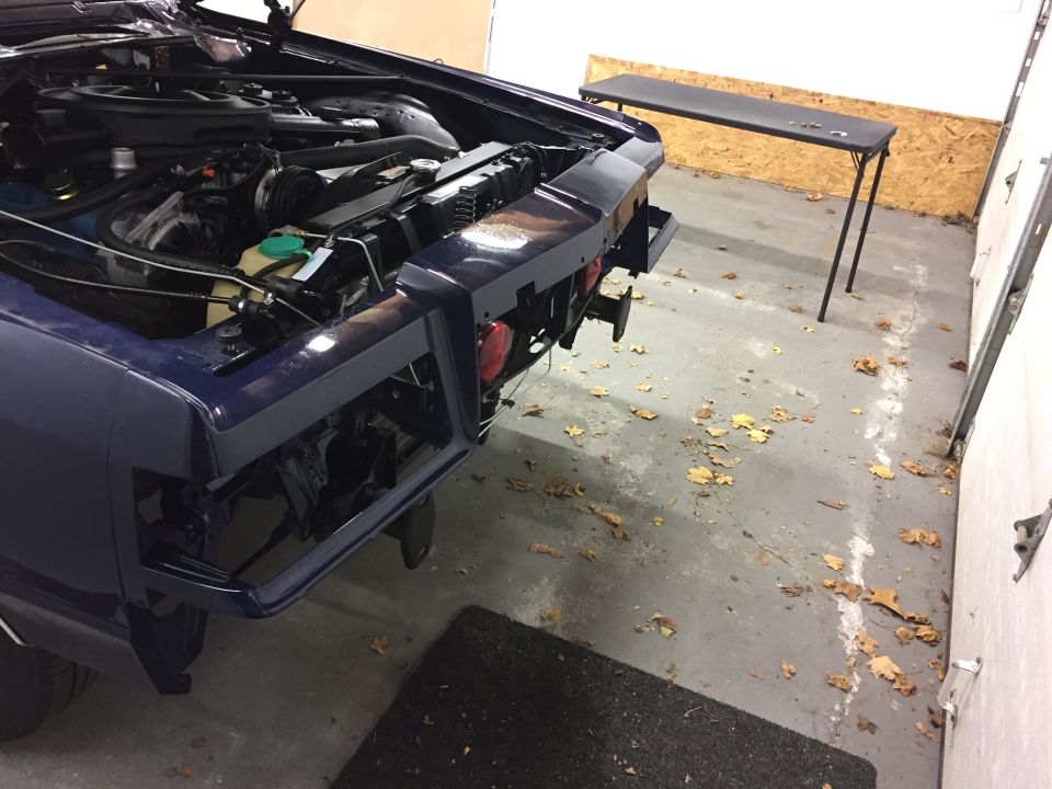 Dark blue car's front end disassembled, hood open, showing engine bay and radiator