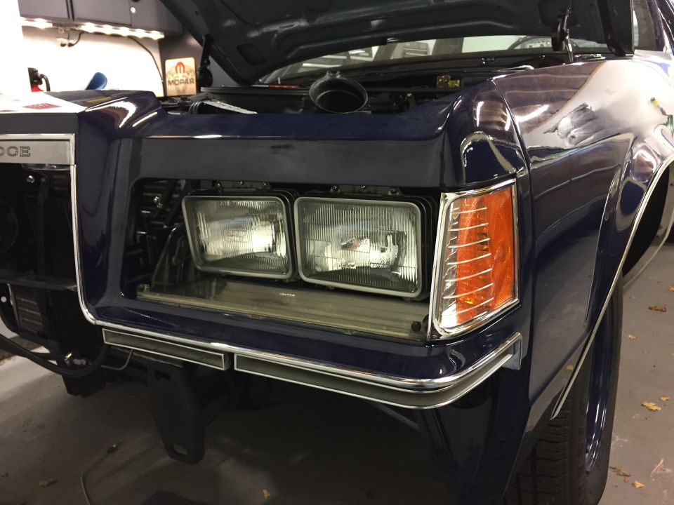 Dark blue car front end with hood open, showing dual headlights and orange turn signals