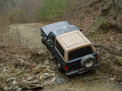 1987 Ford Bronco - A 1987 Ford Bronco navigates a challenging off-road path with a spare tire mounted on the rear.