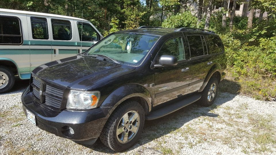 Black SUV parked next to a white van. The SUV has a roof rack and running boards
