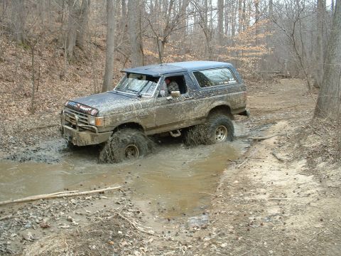 1987 Ford Bronco - This 1987 Ford Bronco navigates a muddy off-road trail, kicking up water as it goes.
