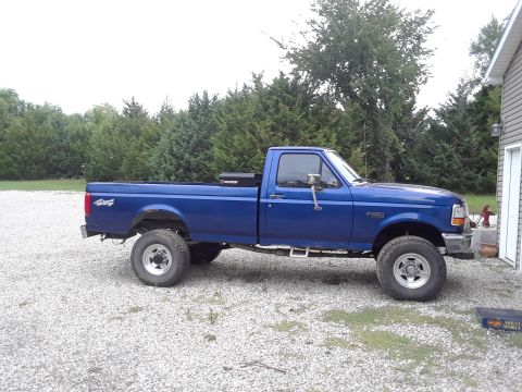 1996 Ford F-350 - This blue 1996 Ford F-350 pickup truck is parked on a gravel lot next to a building.