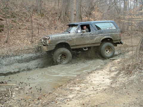 1987 Ford Bronco - Ford Bronco navigating a muddy off-road course in a wooded area.