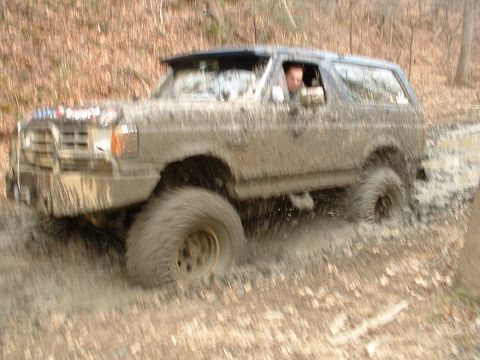 1987 Ford Bronco - This SUV is covered in mud as it navigates through a wet, wooded area.