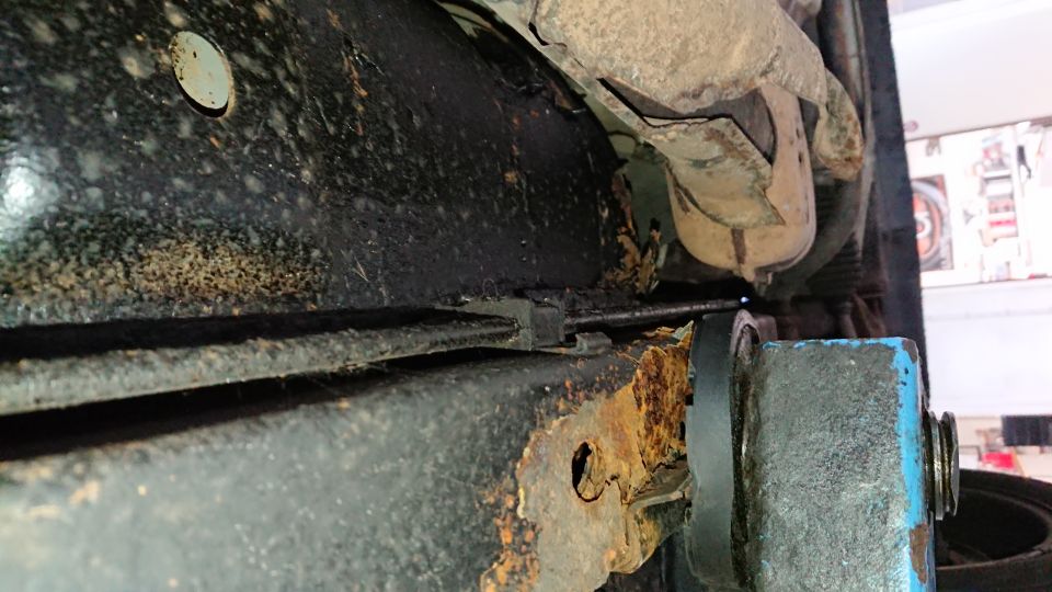 Undercarriage frame with extensive rust and black undercoating. A cable runs along the frame