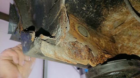 1999 Ford Fairlane - Close-up of severe rust damage on a vehicle's undercarriage, with a hand indicating the extent of corrosion.