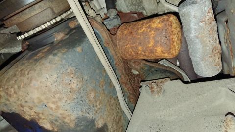 1999 Ford Fairlane - Close-up view of heavily rusted exhaust pipe and undercarriage parts.