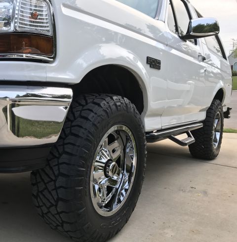 1995 Ford Bronco - Front quarter view of a white 1995 Ford Bronco with custom chrome wheels and side steps.